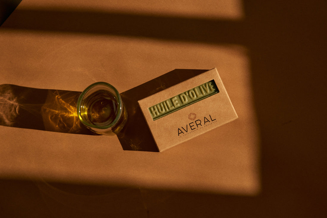 Averal Provence Olive Oil bar soap in its kraft box beside a glass of olive oil in warm light