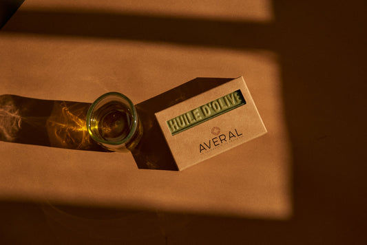Averal Provence Olive Oil bar soap in its kraft box beside a glass of olive oil in warm light